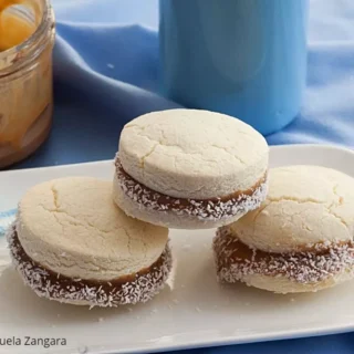 Alfajores de Maicena with Dulce de Leche filling and coconut edges, placed beside a jar of caramel.
