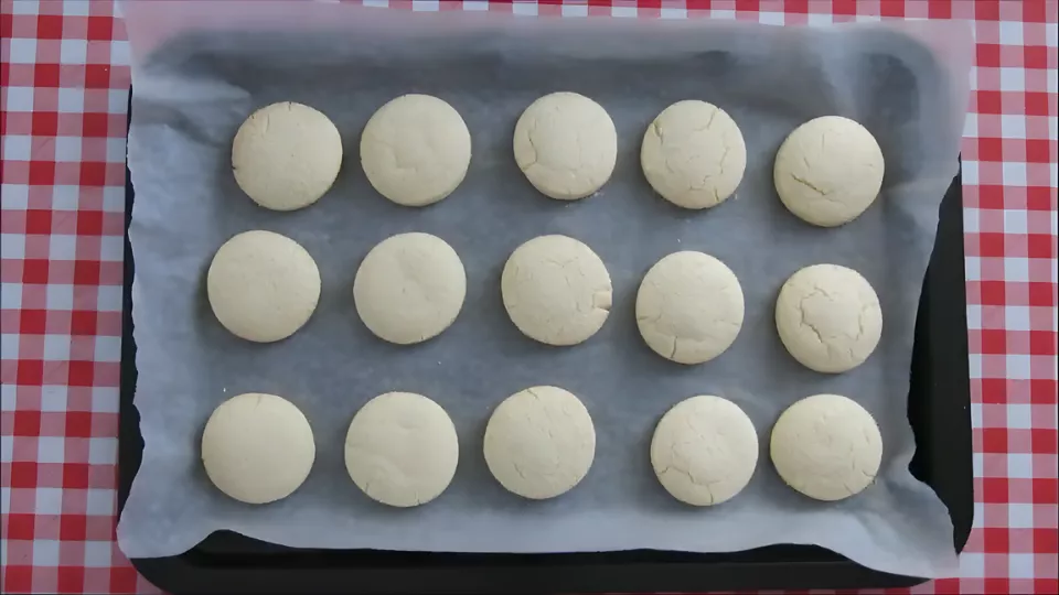 Freshly baked alfajores cookies cooling on a tray lined with parchment paper.