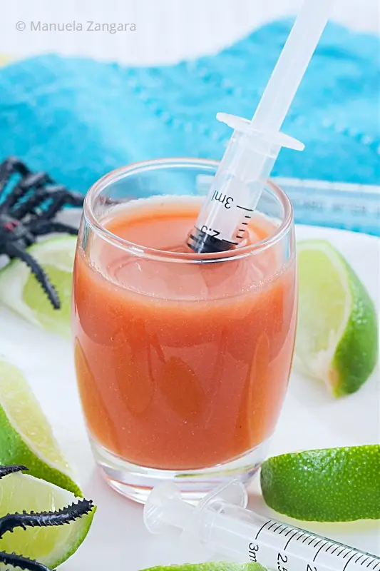 Close-up Bloody Mary shot in a glass with syringe and lime.