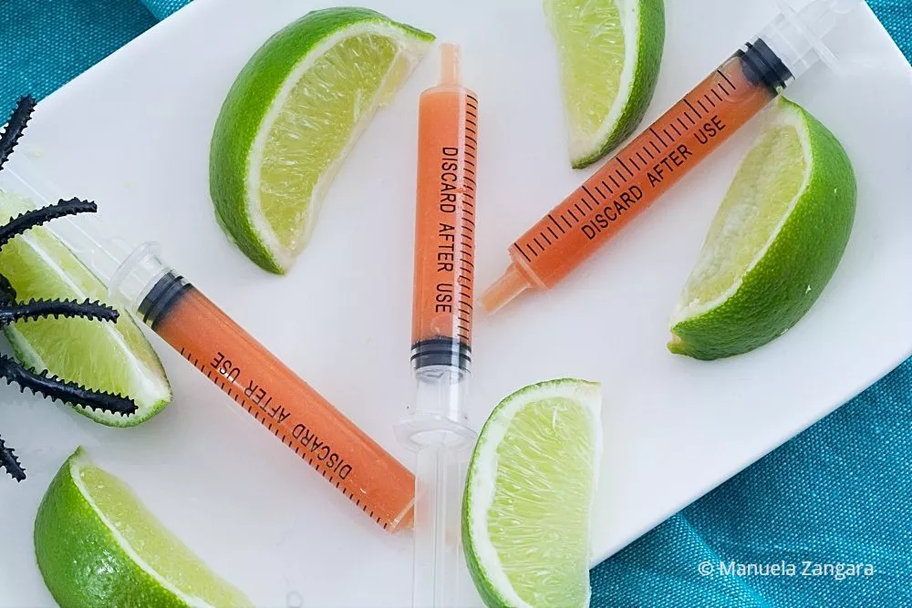 Close-up of Bloody Mary shots in syringes with lime wedges.