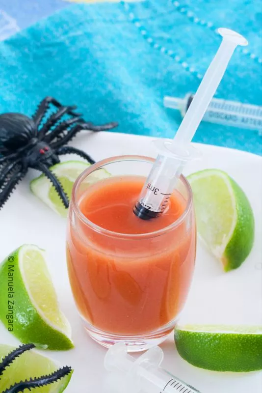 Bloody Mary shot in a glass with syringe and decorative spider.