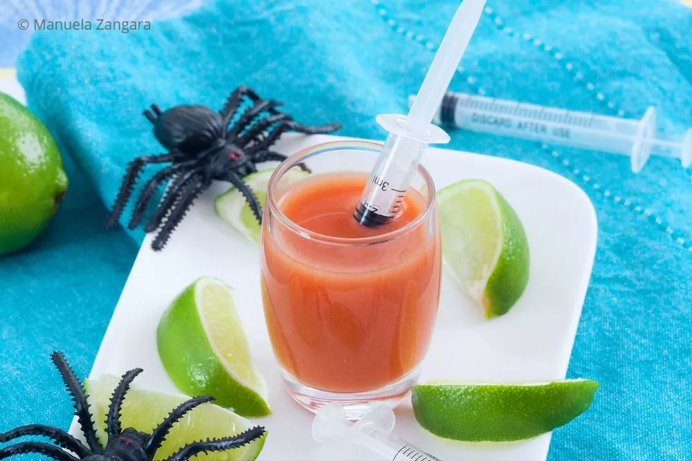Bloody Mary shot in a glass with syringe and lime wedges.