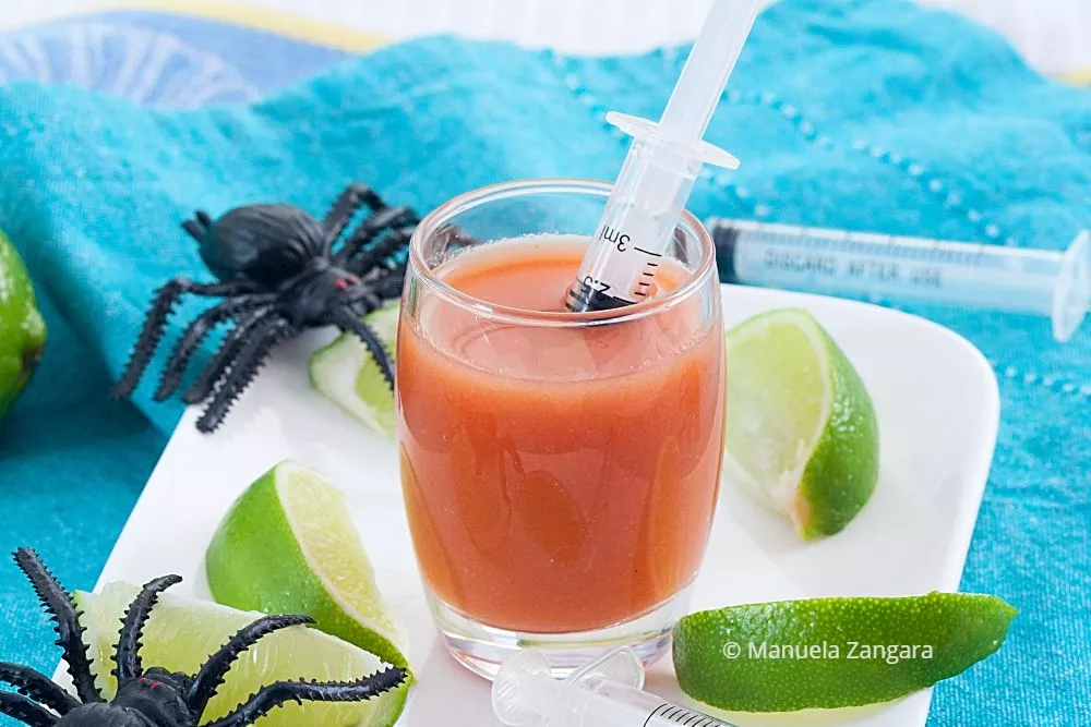 Bloody Mary shot in a glass with syringe and Halloween decor.