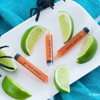 Syringes filled with Bloody Mary on a plate with lime wedges.