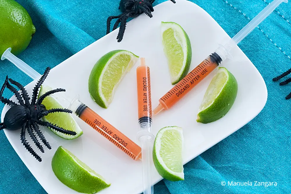 Syringes filled with Bloody Mary on a plate with lime wedges.