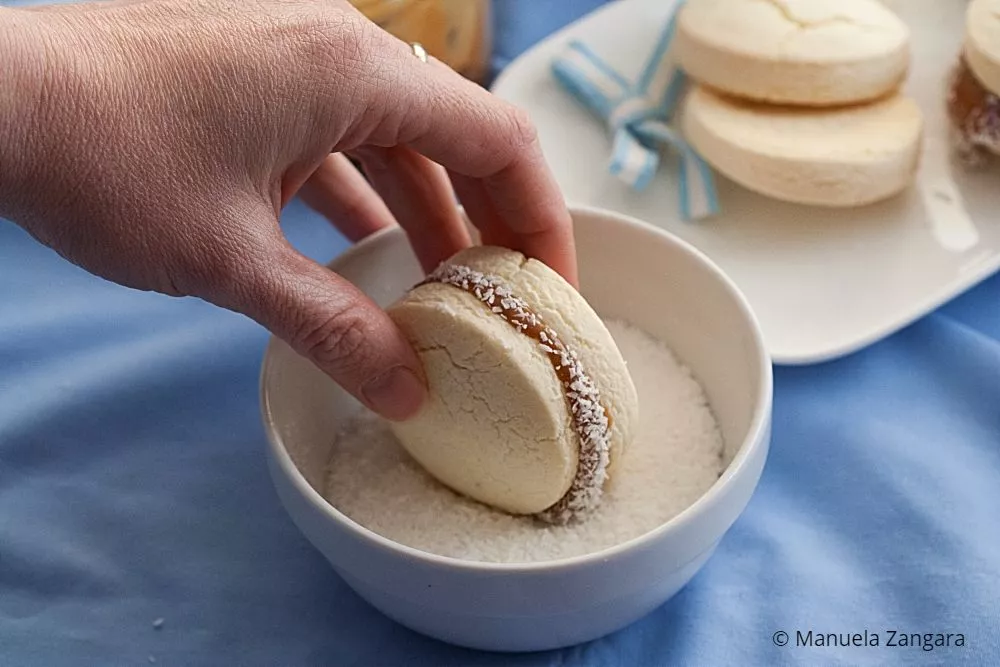 Hand coating Dulce de Leche-filled Alfajores in coconut before serving.