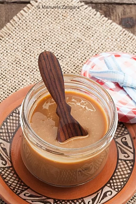 Homemade Dulce de Leche caramel spread in a decorative jar on a table.