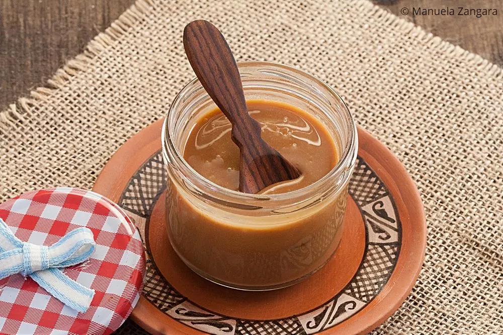 Jar of homemade Dulce de Leche with a wooden spoon on a plate.