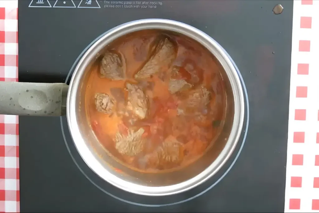 Beef simmering in a pot with tomato sauce.