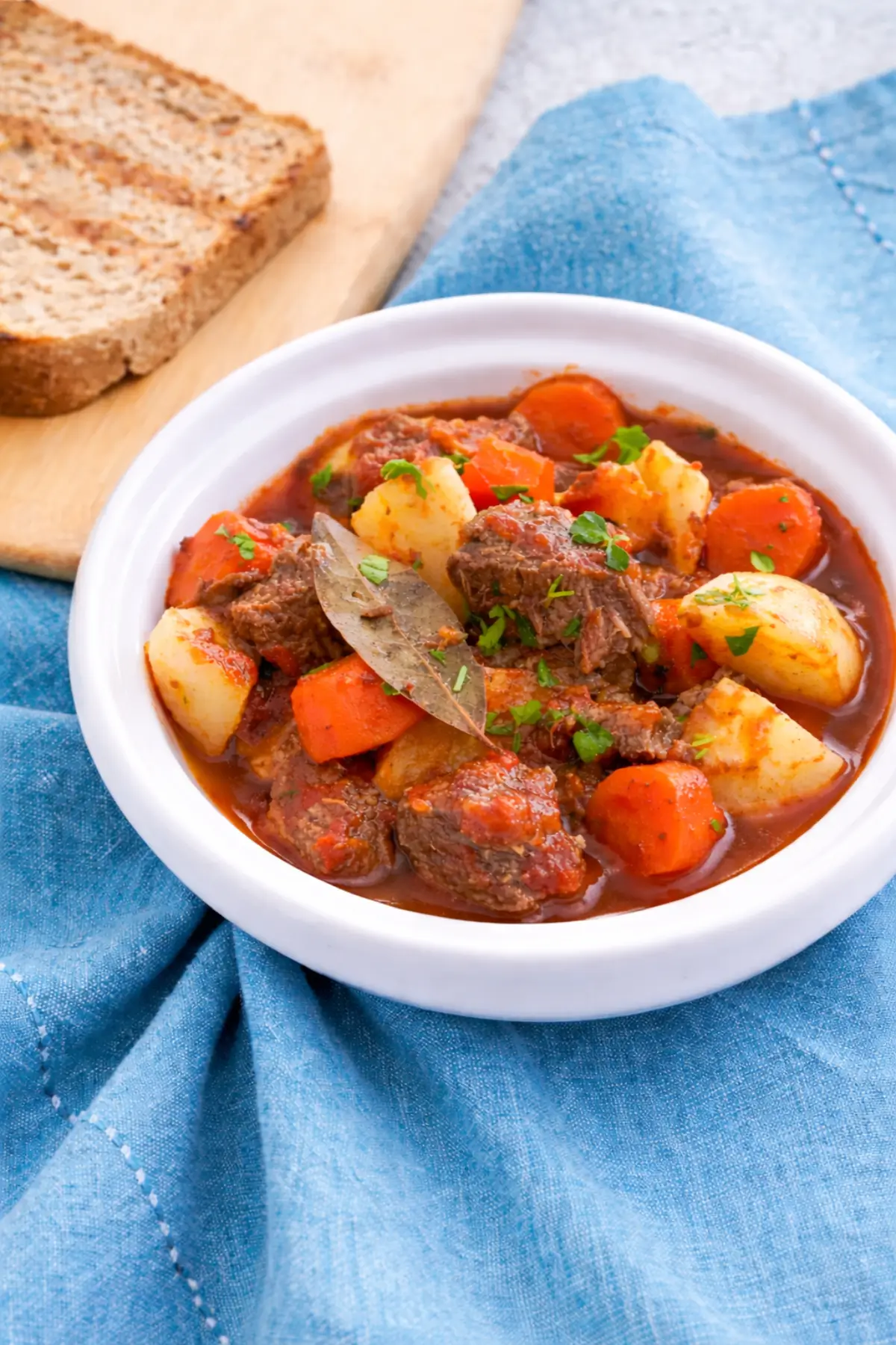 Low FODMAP Beef Stew served in a bowl with carrots, potatoes, and bread on the side.