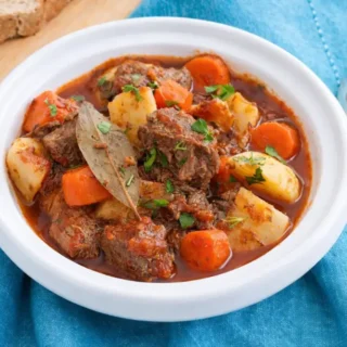Close-up of beef stew with tender meat, carrots, and potatoes in sauce.