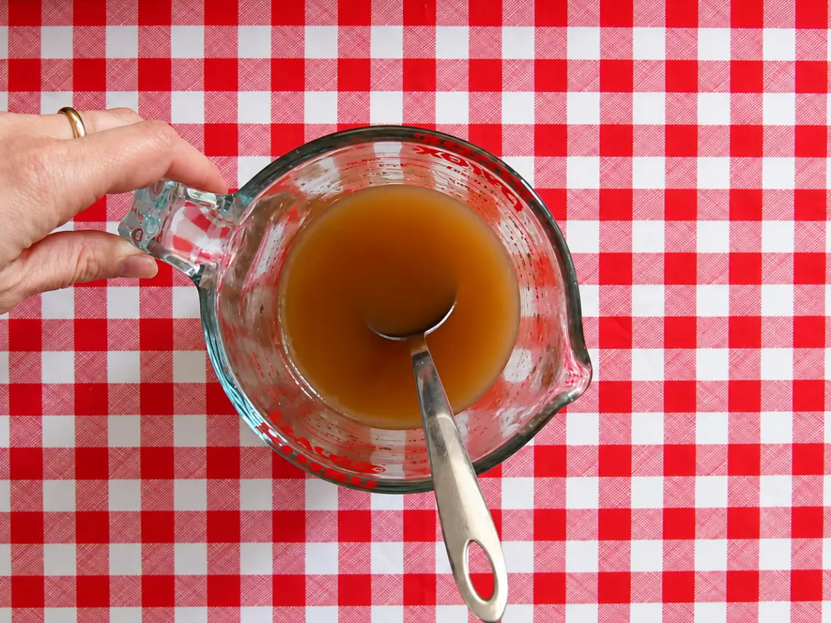 Measuring jug filled with chicken broth, soy sauce, and rice wine vinegar before warming.