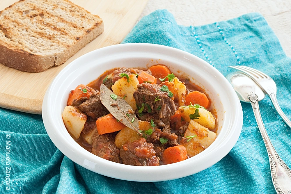 Bowl of beef stew with carrots and potatoes.