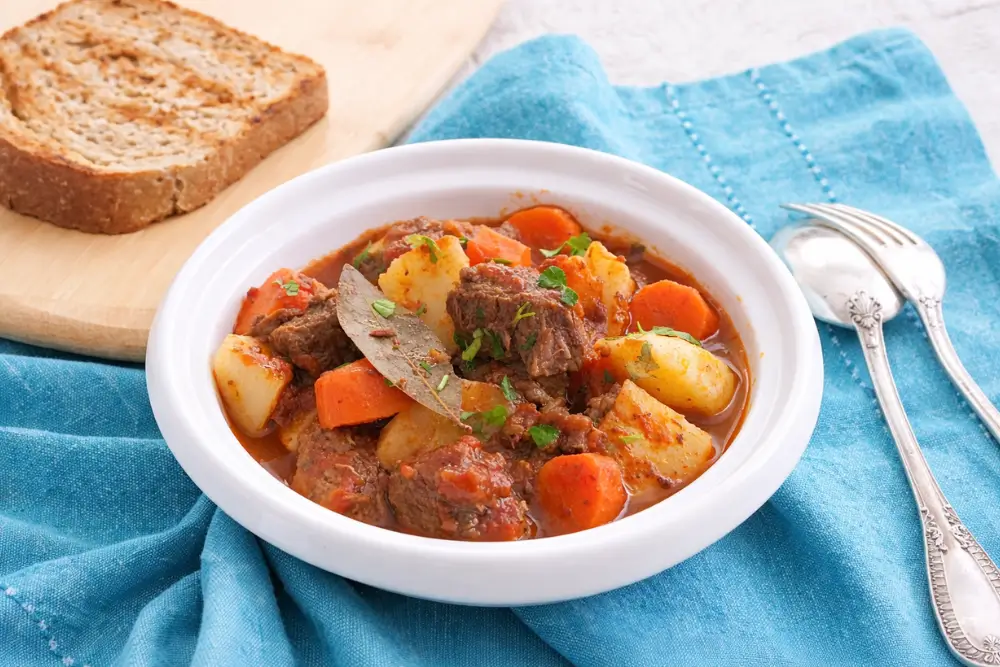Low FODMAP Beef Stew served in a bowl with carrots, potatoes, and a slice of bread on the side.