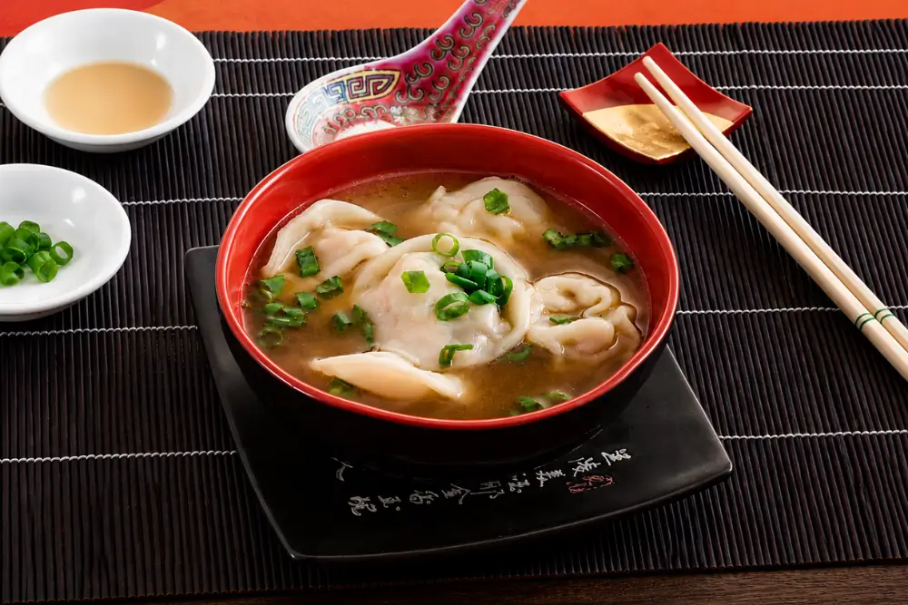 Bowl of Low FODMAP wonton soup topped with sliced green onion in a red serving bowl.