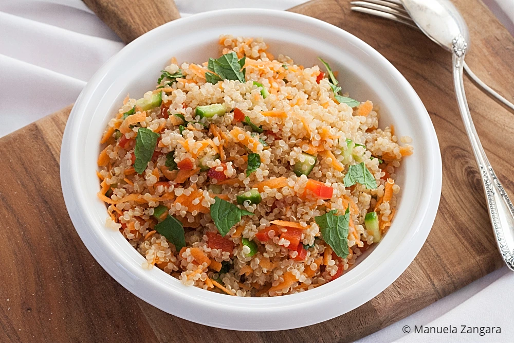 Overhead view of quinoa salad in a white bowl on a wooden board.