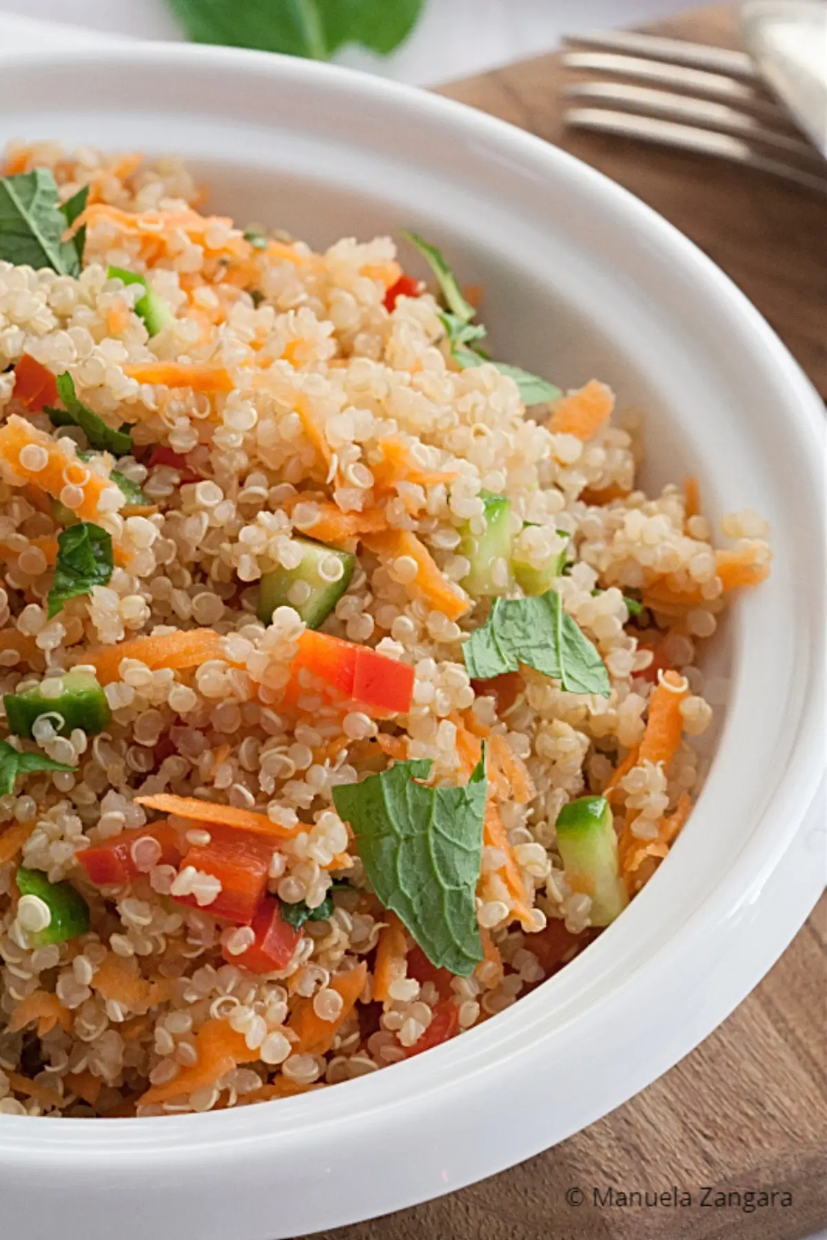 Bowl of quinoa salad with grated carrot, cucumber, red capsicum and mint.