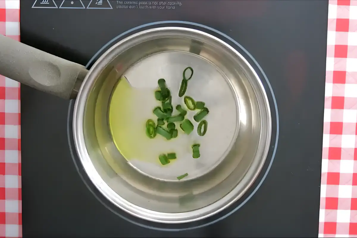 Spring onion tops sautéing in olive oil in a pot.