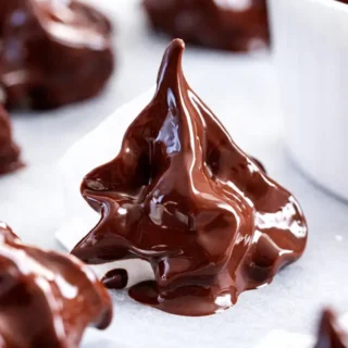 Chocolate Meringues coated in melted chocolate with glossy finish on parchment-lined tray.