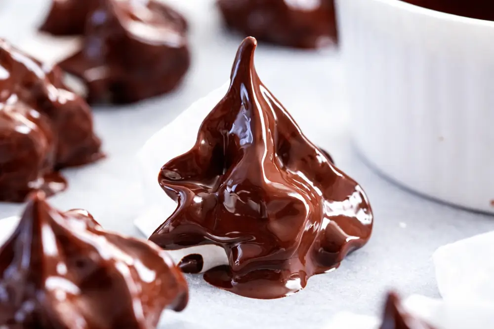 Chocolate Meringues coated in melted chocolate with glossy finish on parchment-lined tray.