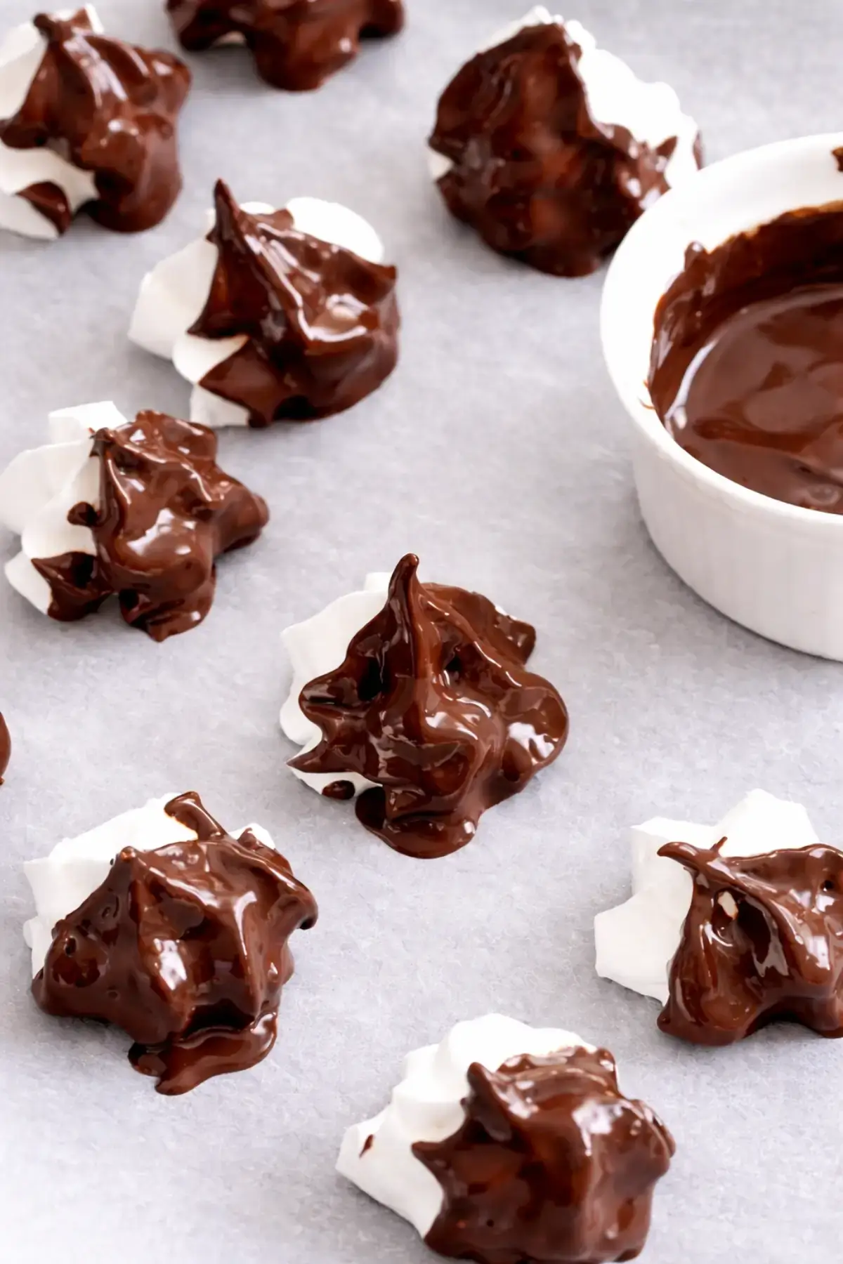 Chocolate Meringues dipped in melted chocolate with a glossy finish on a baking surface.