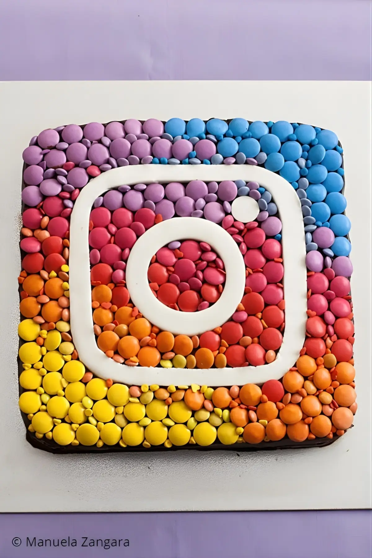 Top view of Instagram Cake decorated with rainbow Smarties and white fondant logo.