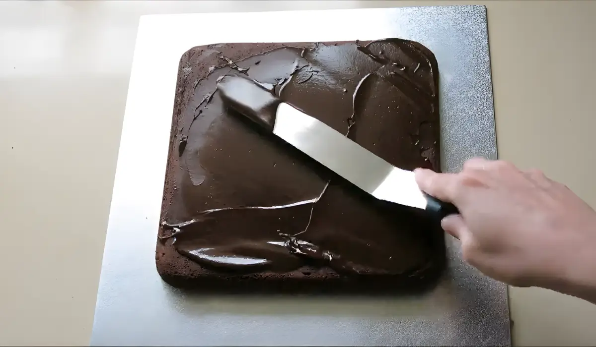 Spreading chocolate ganache evenly over brownie cake with offset spatula.