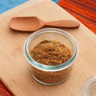 Low FODMAP Taco Seasoning stored in a small glass jar on a wooden board.