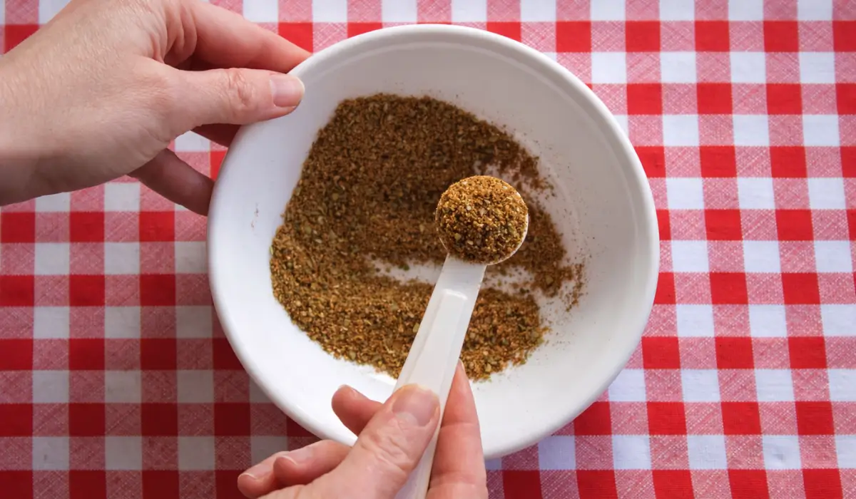 Hand mixing a homemade spice blend in a white bowl with a measuring spoon.