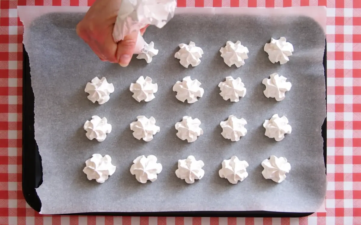 Piped meringues arranged on baking paper on a tray before baking.