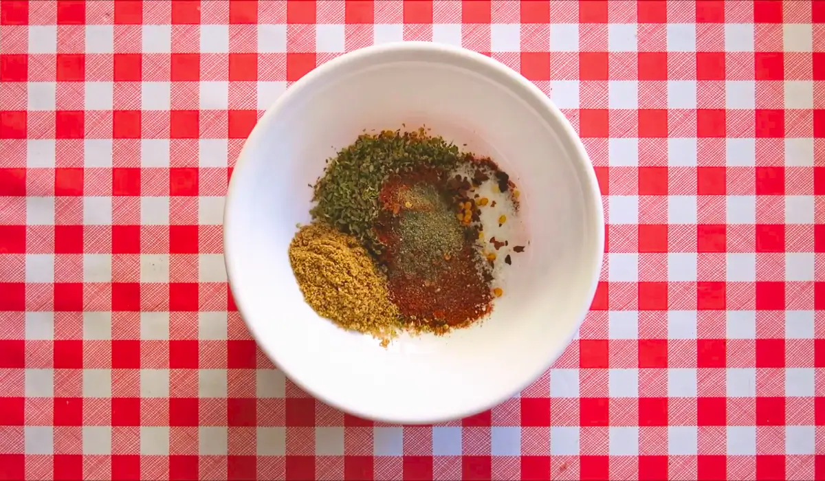 Ground spices measured in a white bowl before mixing on a red check cloth.