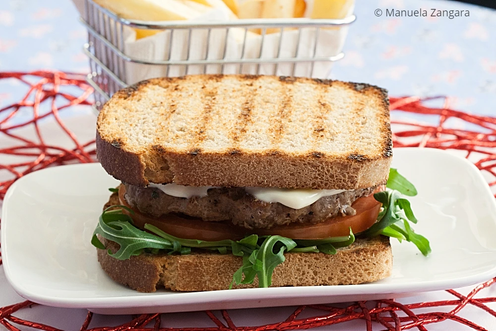 Close-up of a toasted beef burger sandwich with melted aioli and tomato.