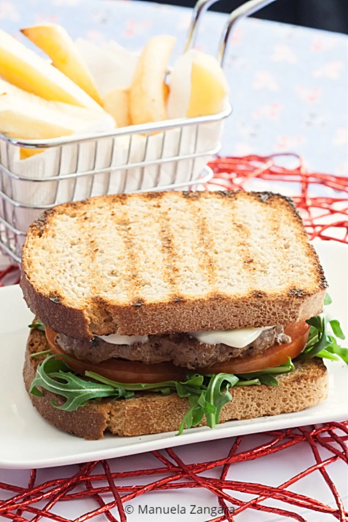 Low FODMAP beef burger on toasted sourdough with rocket, tomato and fries on a white plate.