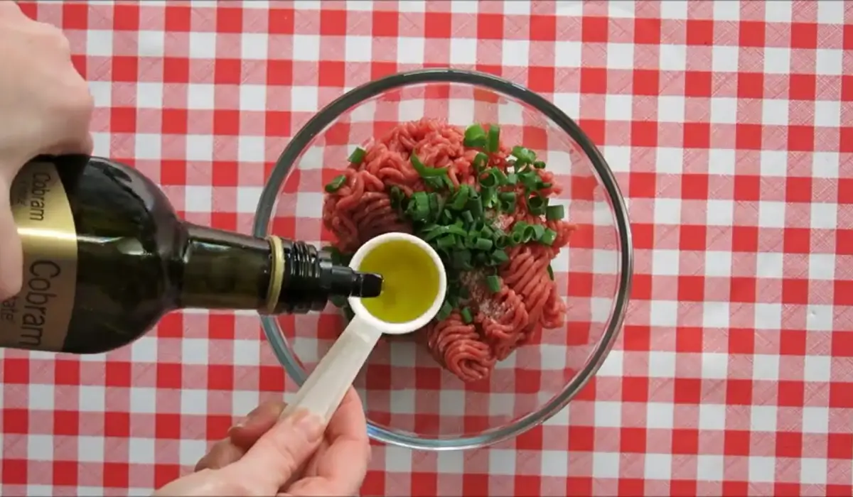 Garlic-infused olive oil being added to mayonnaise in a small bowl.