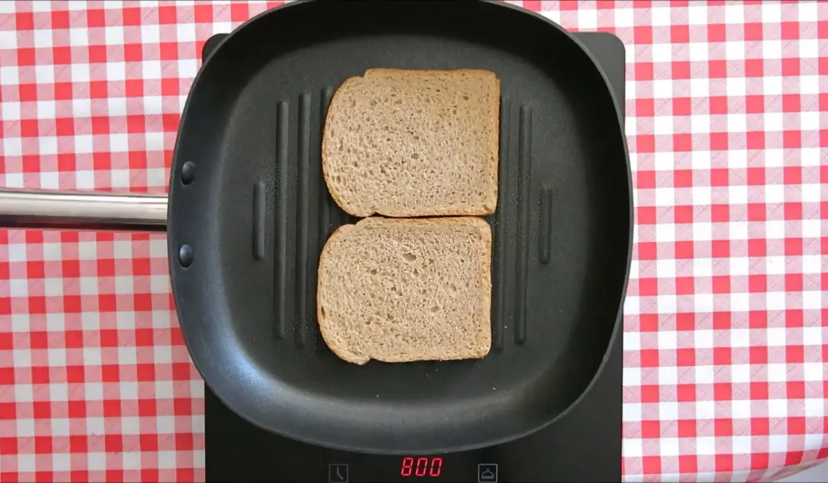Two slices of sourdough bread lightly toasting in a grill pan.
