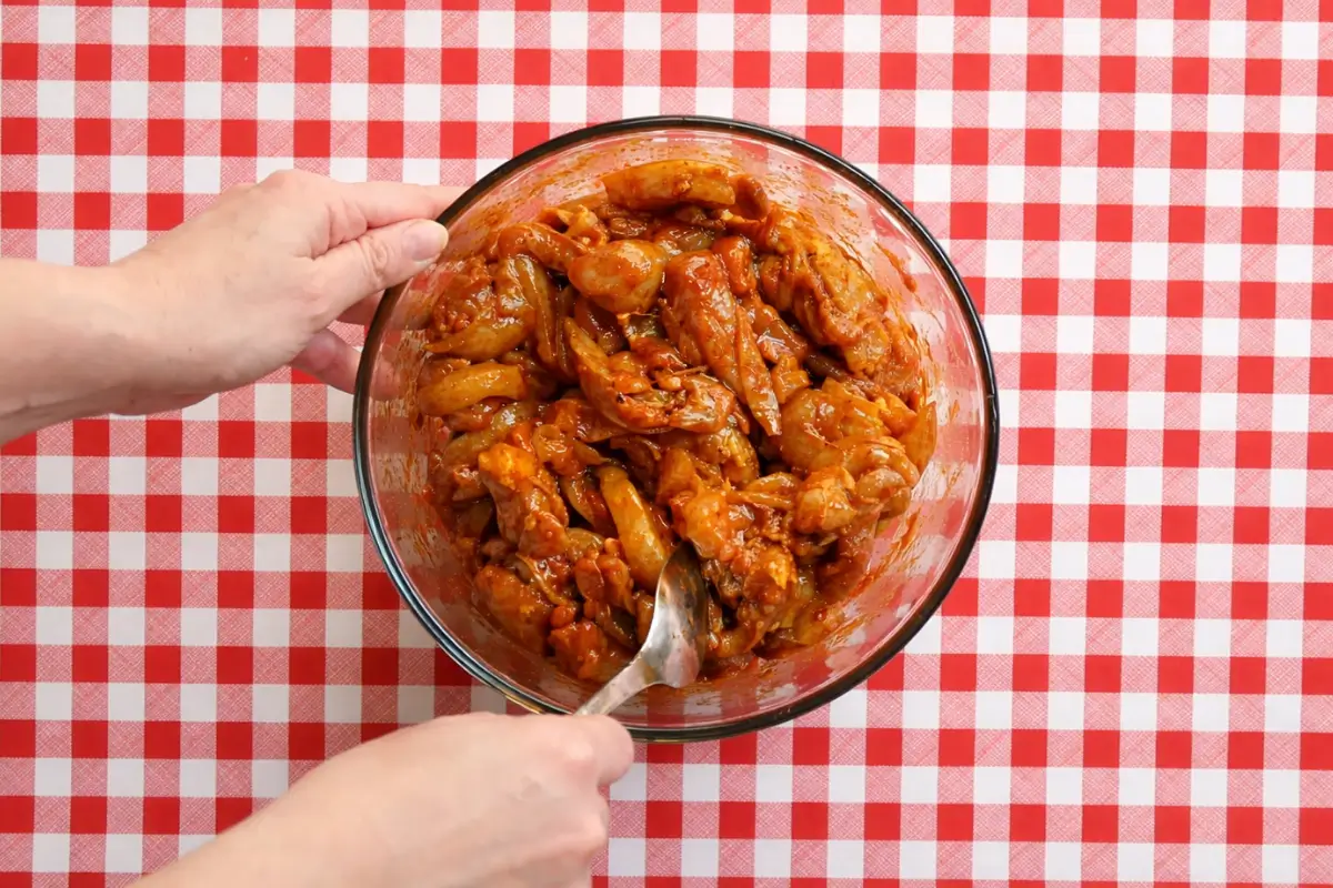 Chicken pieces coated evenly in a paprika marinade in a bowl.
