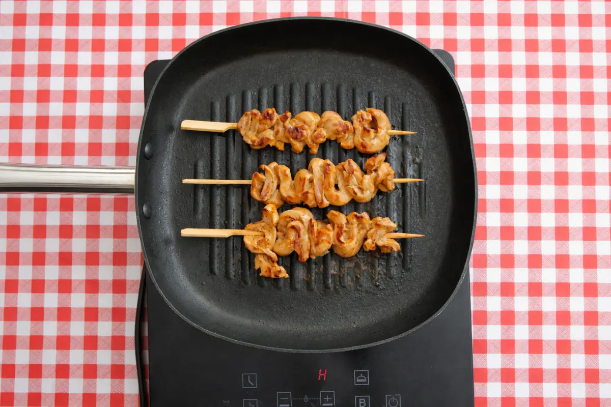 Chicken skewers cooking on a hot griddle with light browning on the surface.