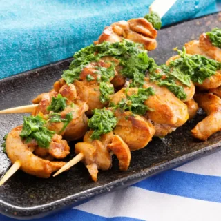 Low FODMAP chicken skewers served with green herb sauce on a plate.