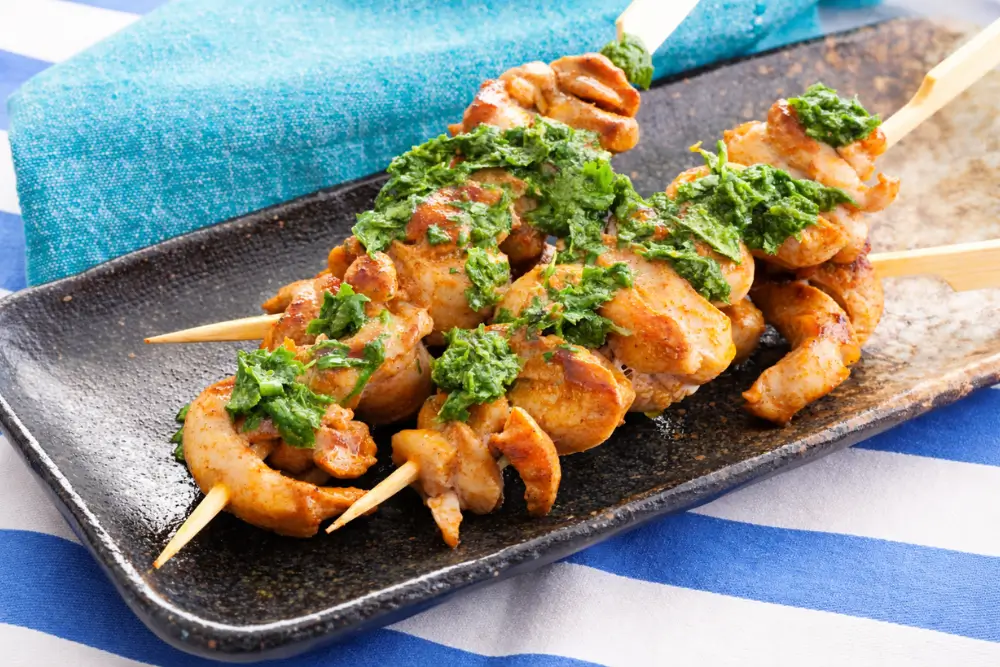 Low FODMAP chicken skewers served with green herb sauce on a plate.