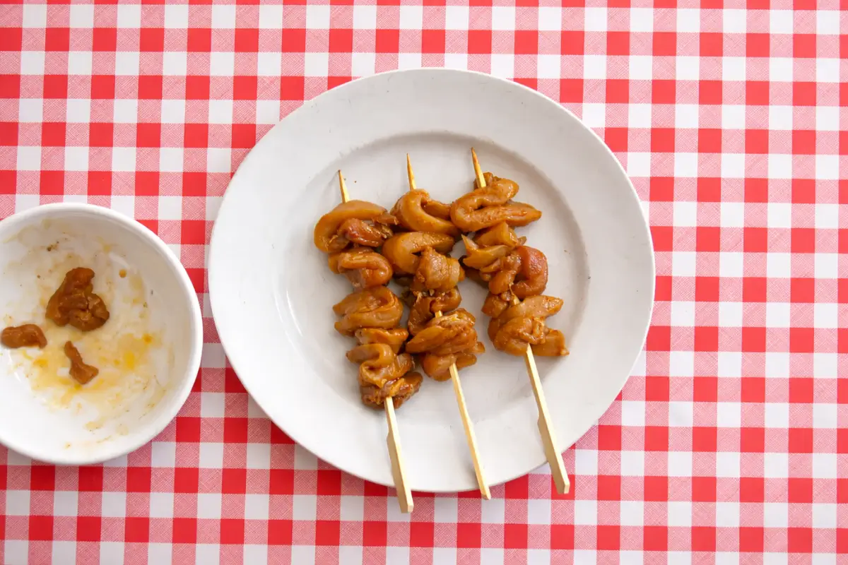 Marinated chicken threaded onto wooden skewers resting on a plate before cooking.