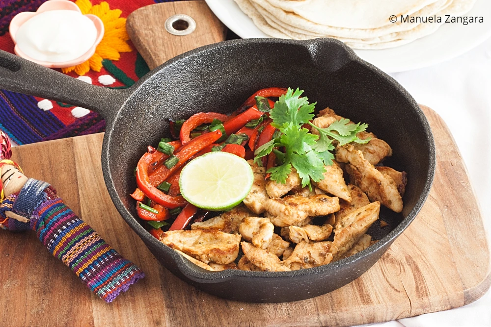 Close-up of chicken fajitas with red capsicum and coriander in a skillet.