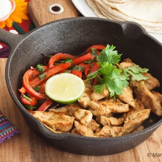 Chicken fajitas in a skillet with capsicum, lime, and coriander.
