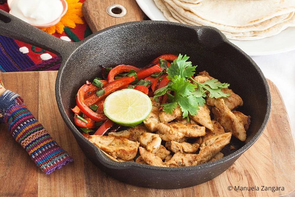 Chicken fajitas in a skillet with capsicum, lime, and coriander.