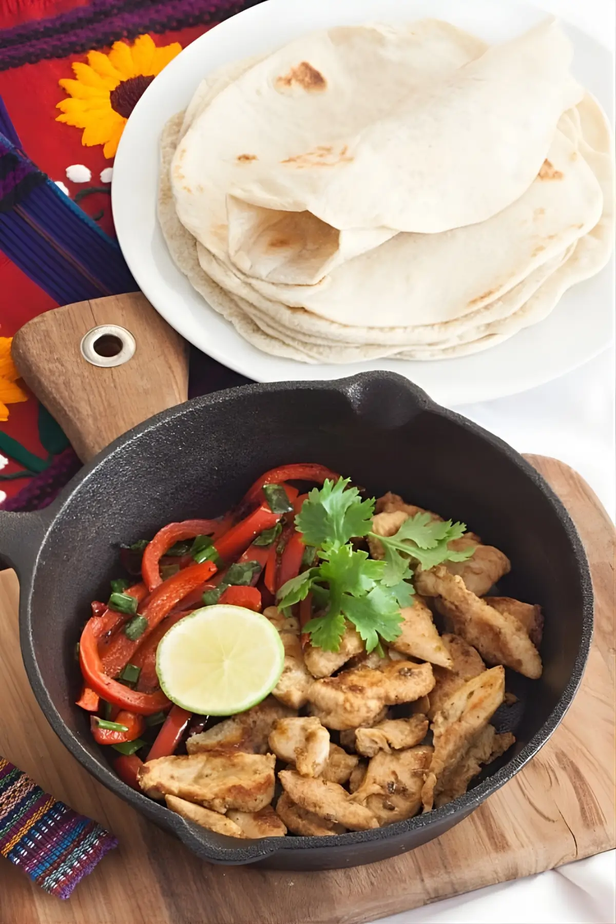 Skillet with cooked chicken and red capsicum served with fresh coriander and lime.
