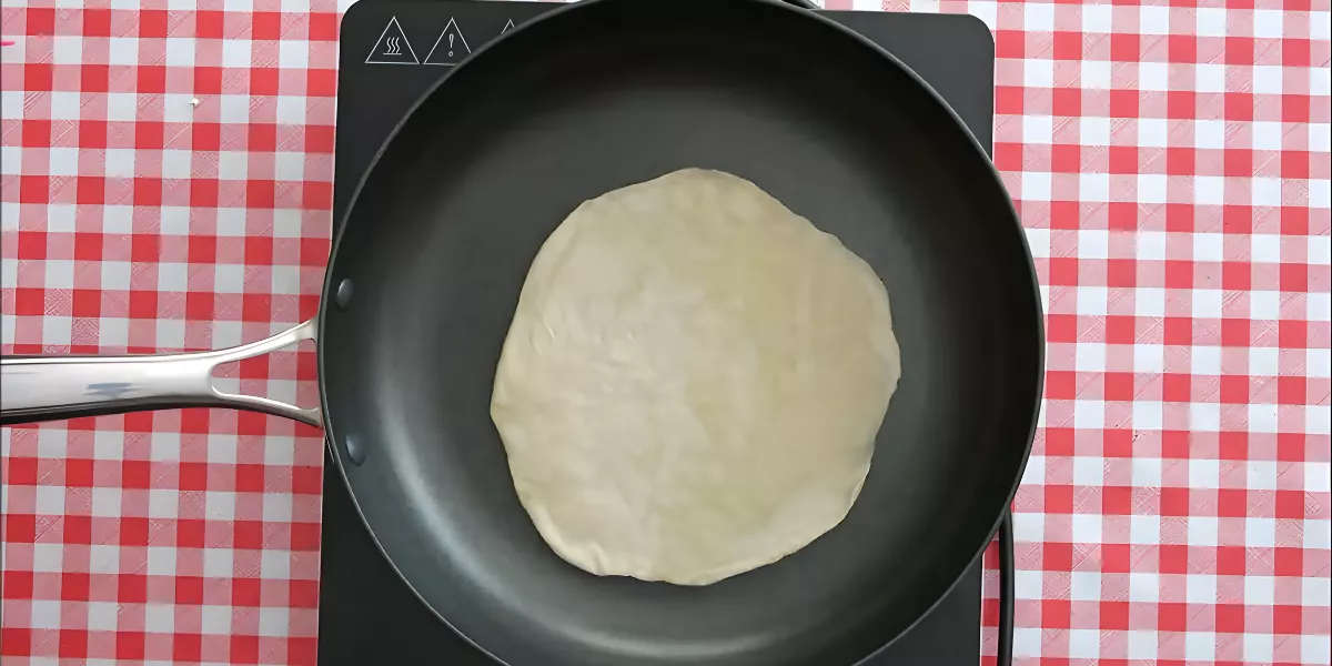 Cooking a Low FODMAP tortilla in a non-stick pan on a red-checked surface.