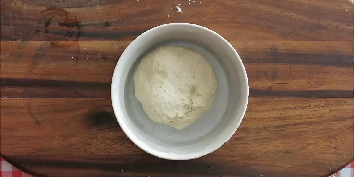 Smooth tortilla dough resting in a bowl on a wooden board.