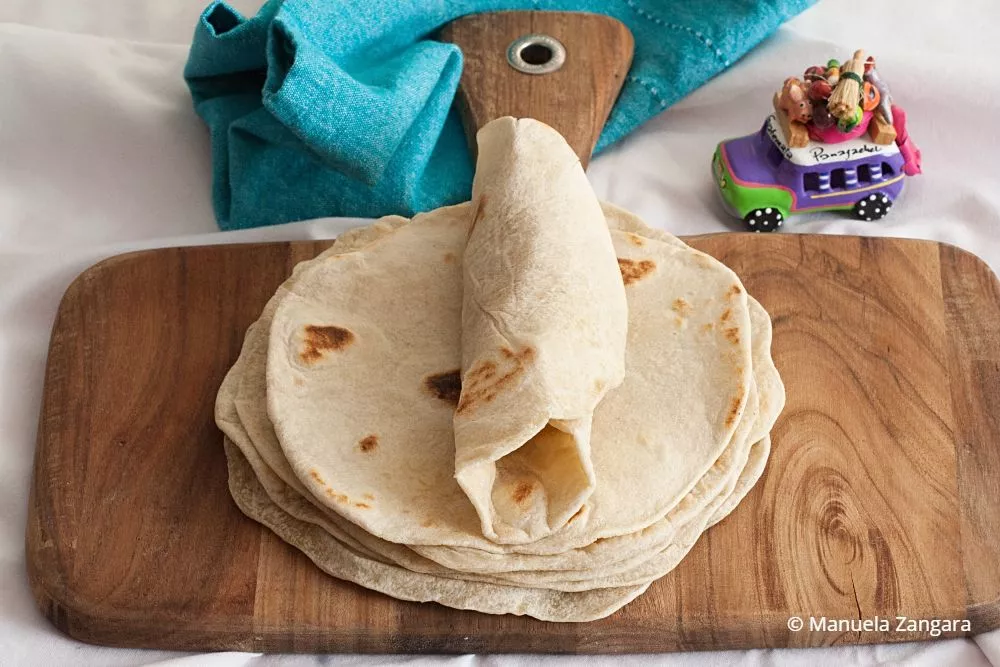 Warm tortillas stacked on a wooden board.
