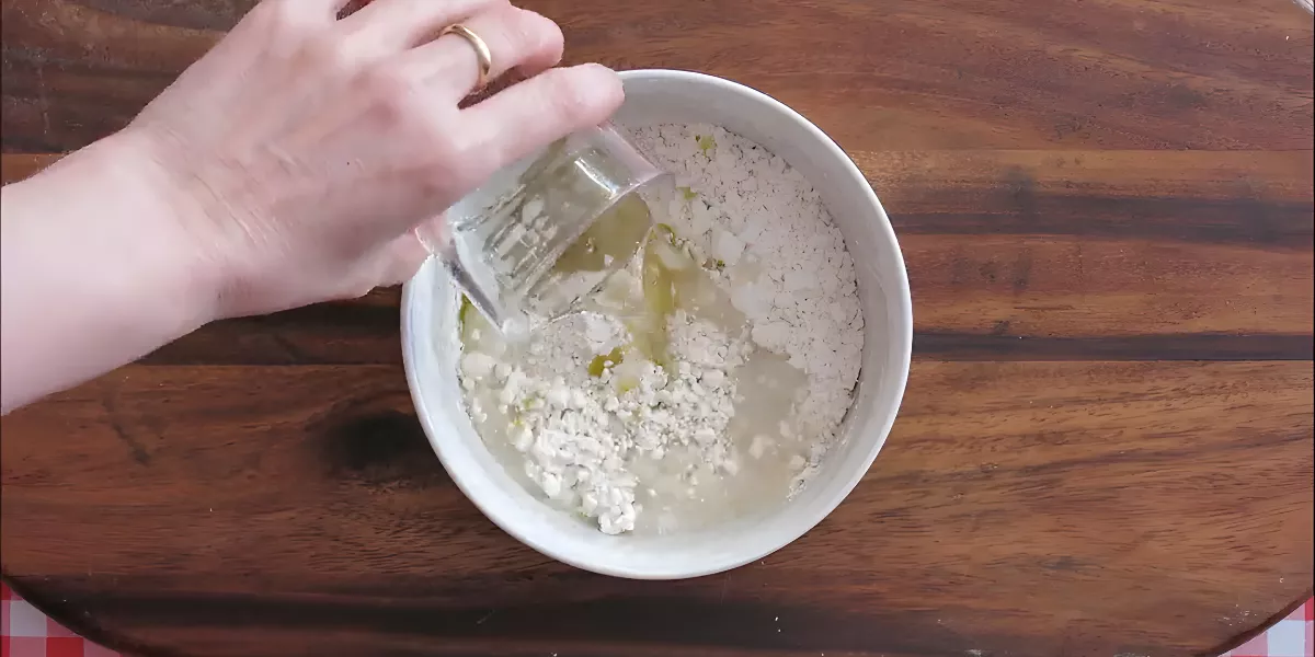 Pouring water into a bowl of flour and olive oil to make tortilla dough.