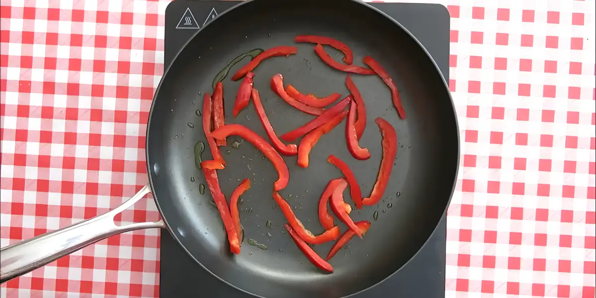 Red capsicum strips sautéing in a pan.