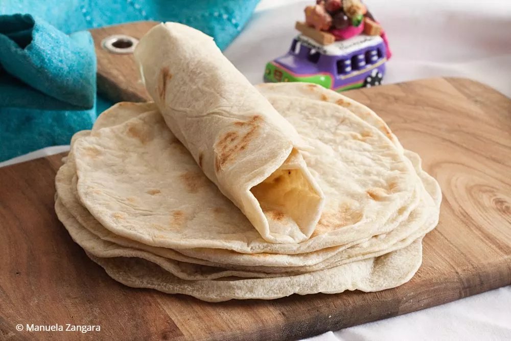 Folded tortilla showing soft texture, stacked on a wooden board.